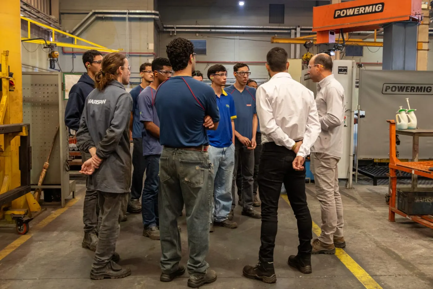Turma do SENAI reunida em roda no chão de fábrica, ao lado de equipamentos de solda